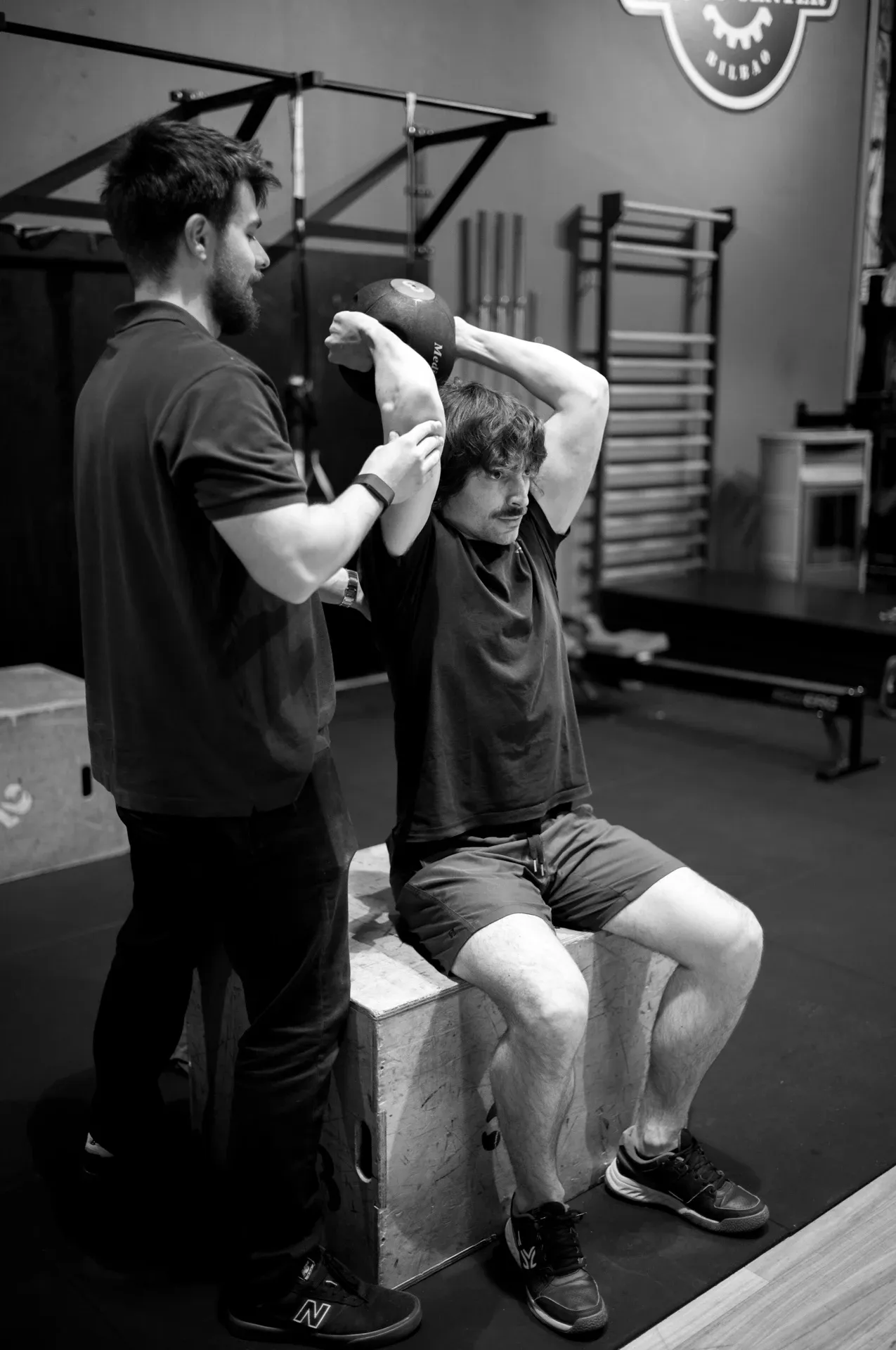 Entrenamiento guiado: coaching a un paciente sentado en el gimnasio, blanco y negro, en la clínica de Iñigo Goikoetxea, fisioterapeuta en Bilbao